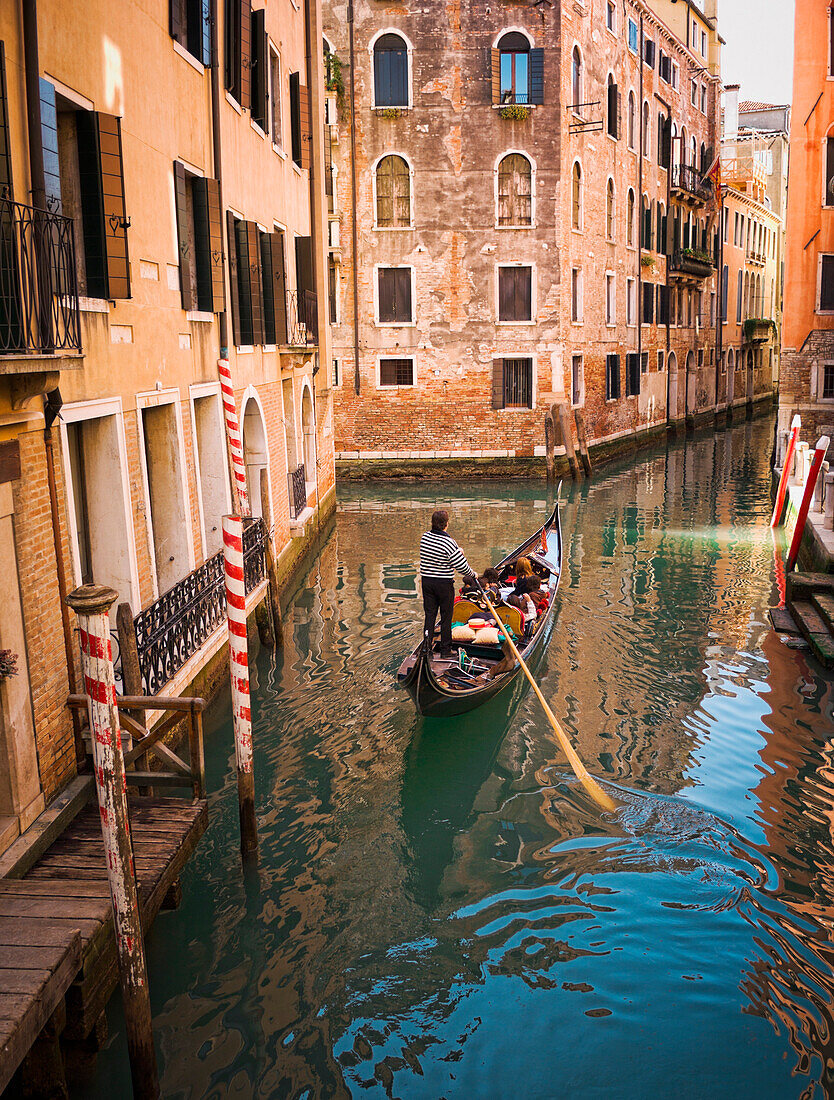 Gondolier rowing gondola in canal, Venice, Venezia, Italy