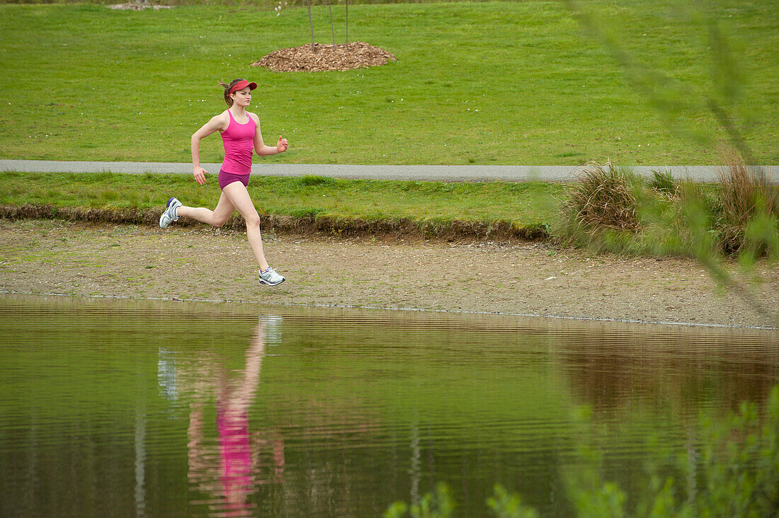 Gemischtrassige Frau, die in der Nähe eines Teiches läuft, Bainbridge Island, WA, Vereinigte Staaten