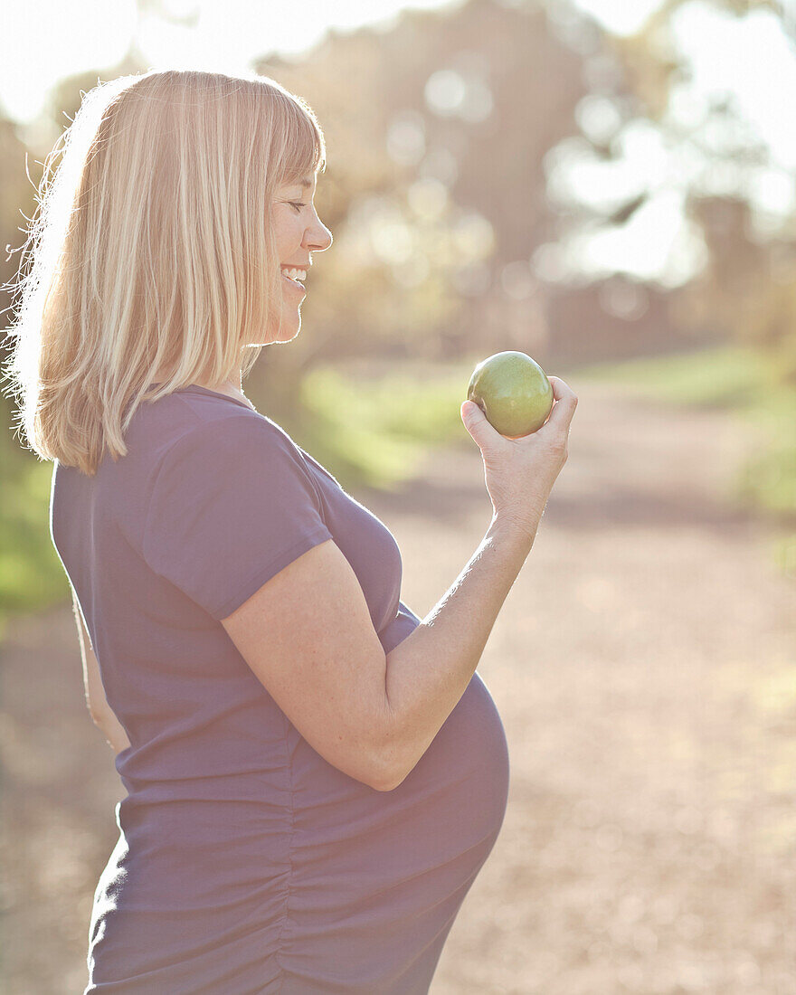 Schwangere kaukasische Frau isst Apfel im Freien, Manhattan Beach, Kalifornien, USA