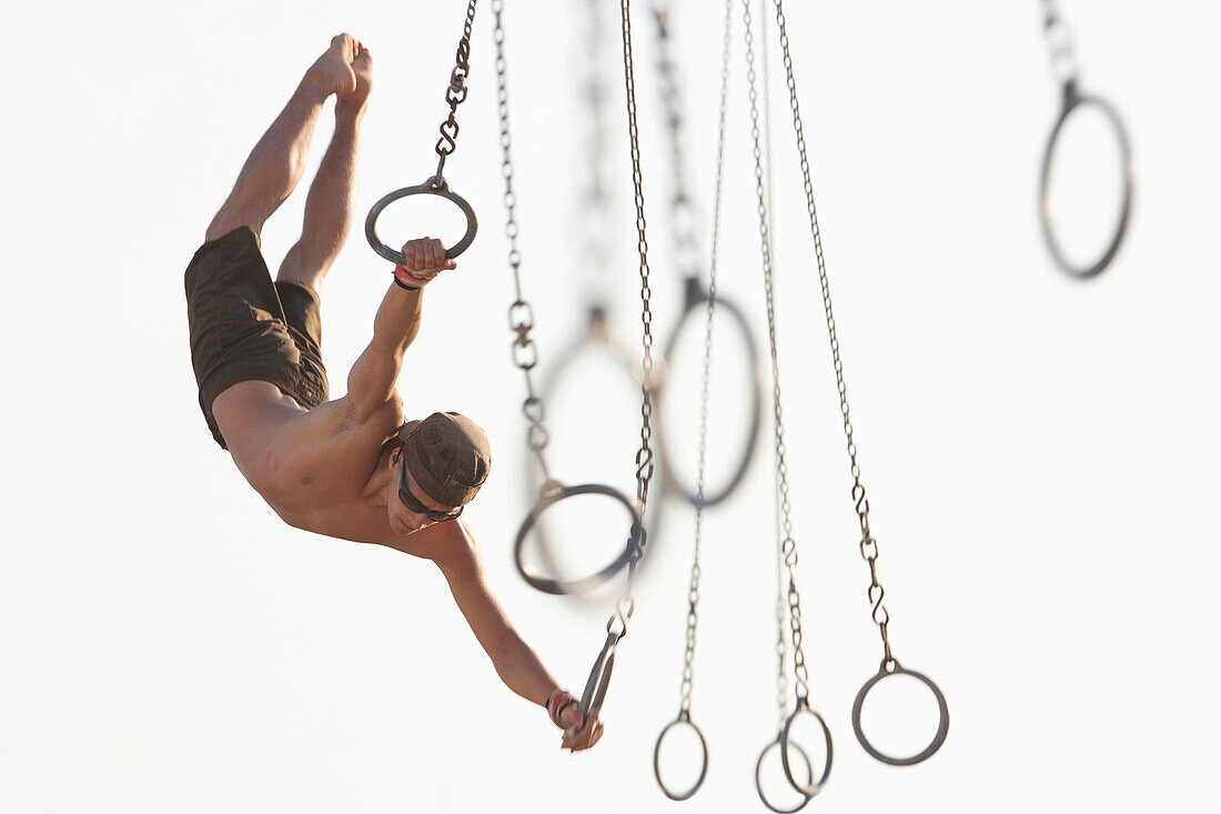 Mixed race man swinging on athletic rings, Santa Monica, California, United States