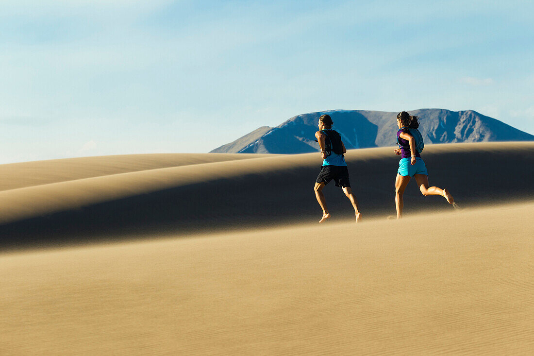 Hispanic couple running on sand dune, Great Sand Dunes National Park, Colorado, USA