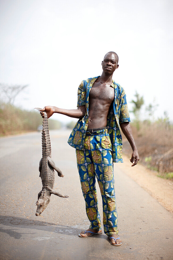 Verkäufer hält ein Krokodil an der Nationalstraße RNE-2, Abomey, Zou, Benin