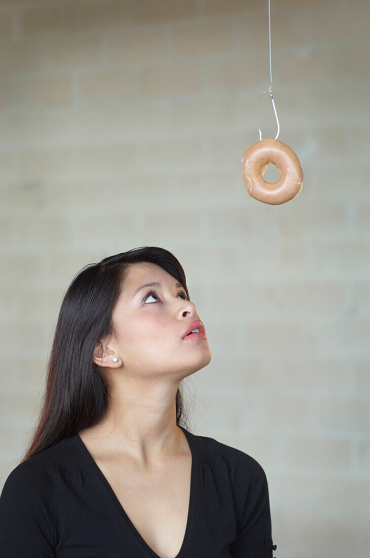 Asian woman looking at doughnut on hook, Richmond, VA