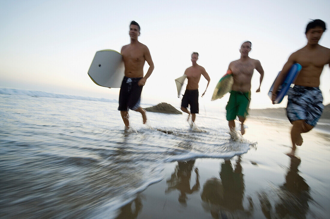 Multi-ethnic men running with surfboards, Newport Beach, CA
