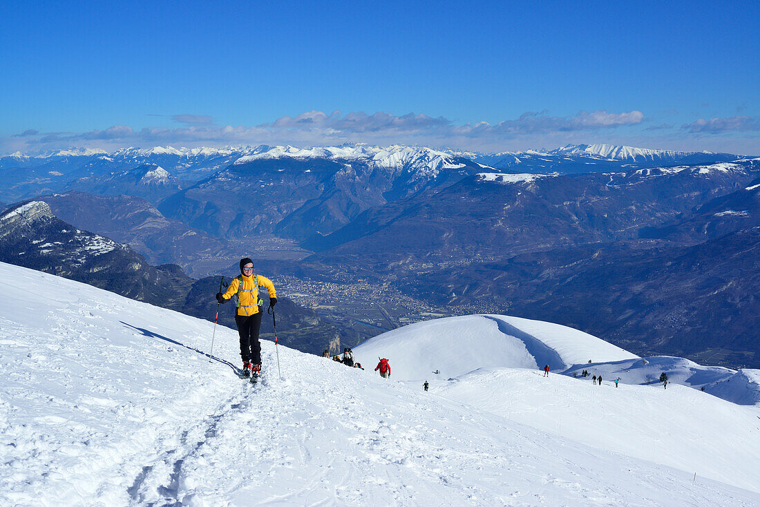 Female back-country skier ascending to Monte Baldo, alpine valley Etschtal in background, Monte Baldo, Garda Mountains, Trentino, Italy