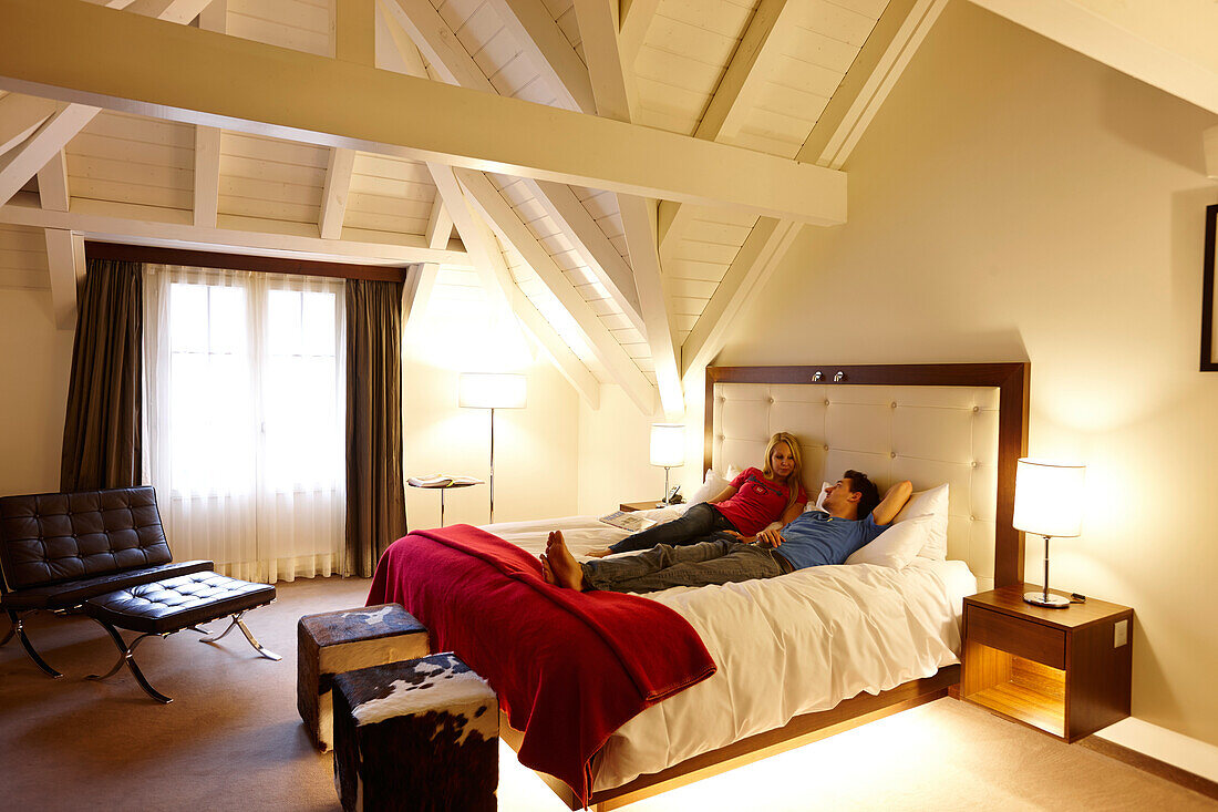 Paar liegt auf einem Doppelbett einer Suite, The Cambrian, Adelboden, Kanton Bern, Schweiz