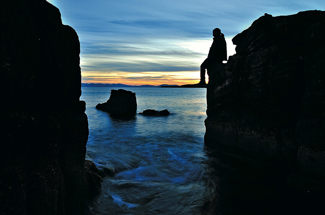 Frau sitzt auf einem Felsen an an der Küste im Sonnenuntergang, Gairloch, Highlands, Schottland, Großbritannien