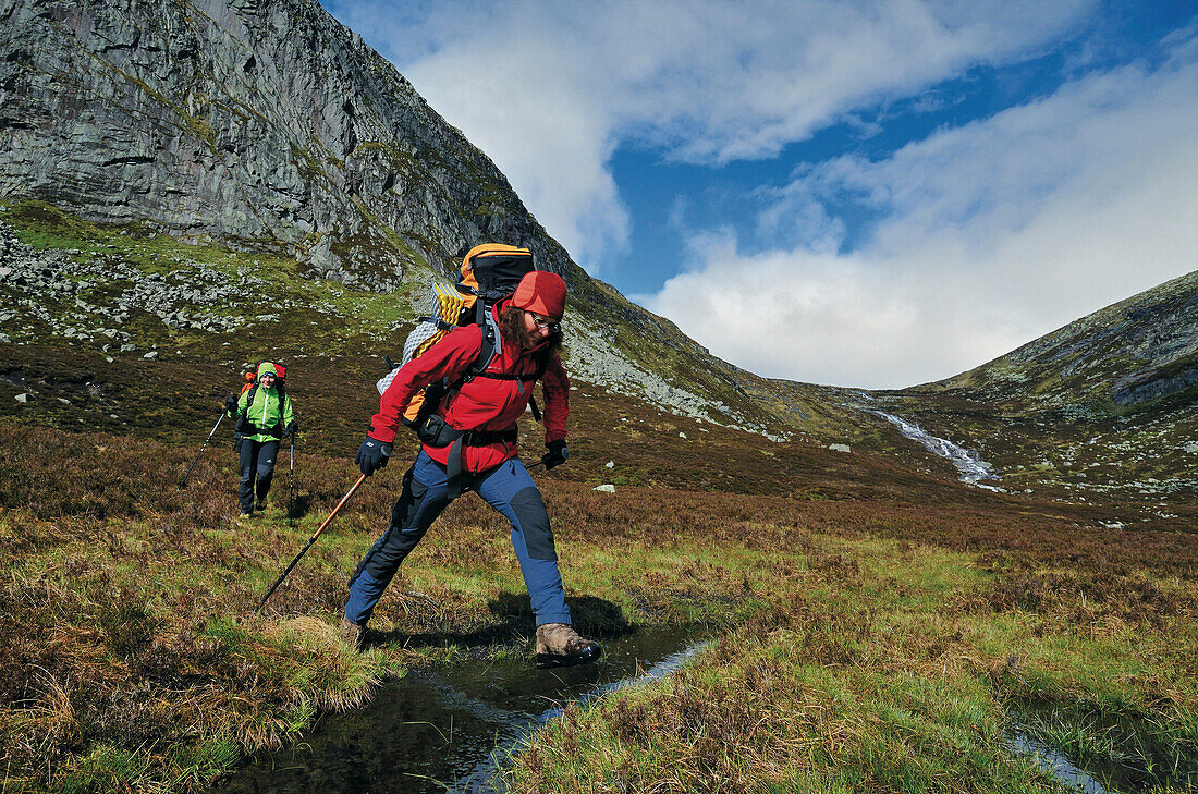 Wanderer springen über einen Bach, Creag an Dubh Loch, Cairngorms, Grampian Mountains, Highlands, Schottland, Großbritannien
