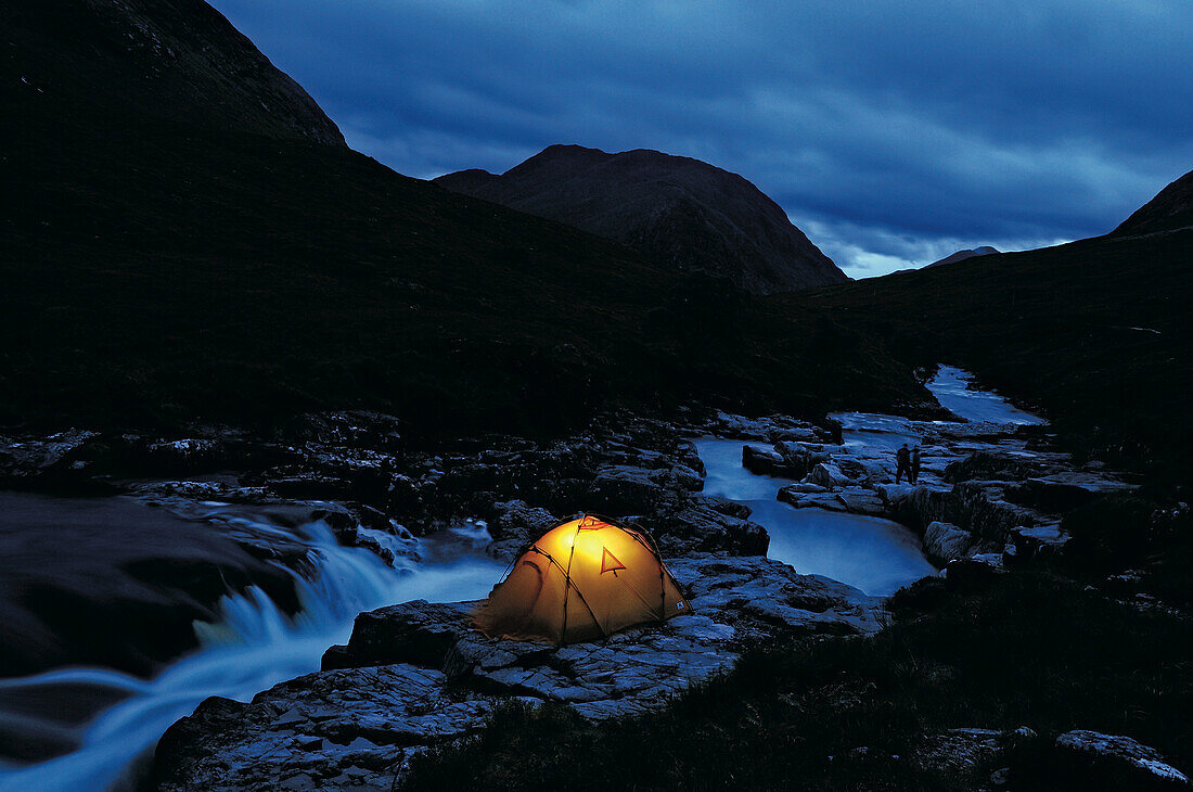 Beleuchtetes Zelt an einem Fluss, Glen Etive, Highlands, Schottland, Großbritannien