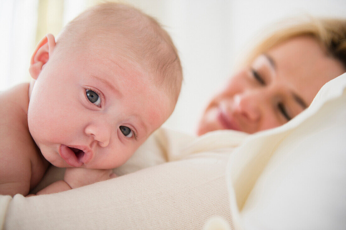 Caucasian mother and baby laying on bed, Jersey City, New Jersey, USA