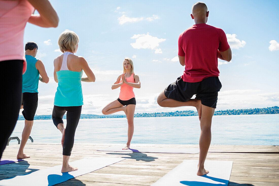 Caucasian people practicing yoga on wooden dock, Seattle, WA, USA