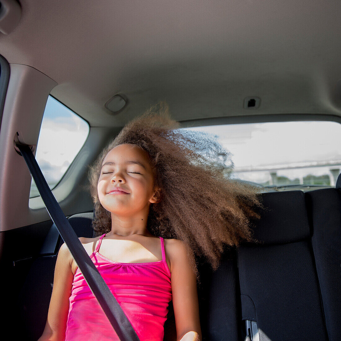 Mixed race girl enjoying wind in hair in back seat of car, Portland, OR, USA