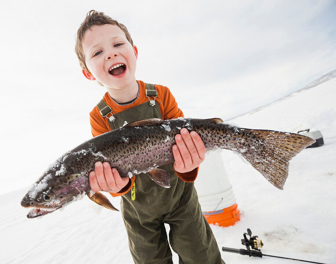 Caucasian boy holding fish in snow, Heber, Utah, USA