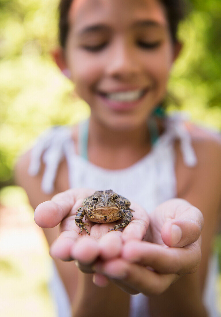 Mixed race girl holding frog outdoors, Huntington Station, New York, USA