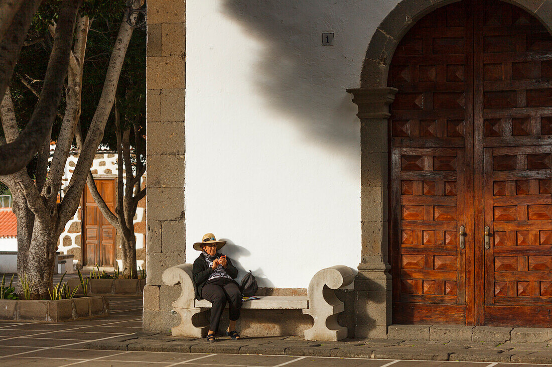 Frau auf einer Bank vor der Kirche, Fataga, Gemeinde San Bartolomé de Tirajana, Gran Canaria, Kanarische Inseln, Spanien, Europa