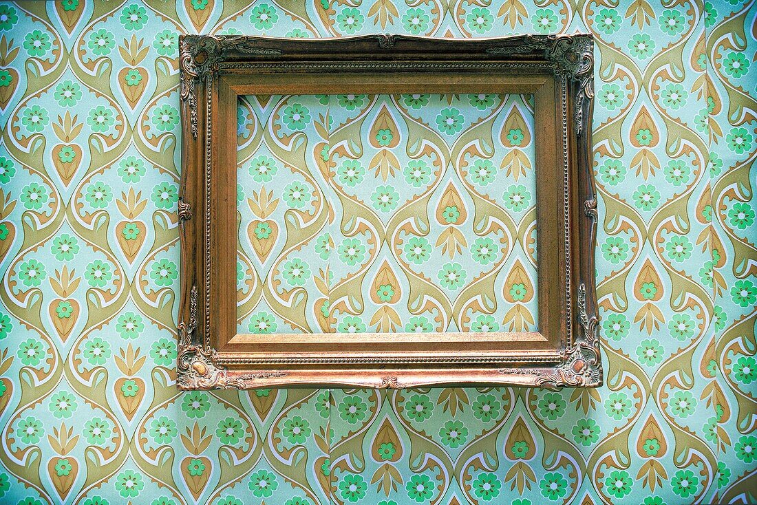 Golden frame, empty, hanging on a wall papered with 70´s paper