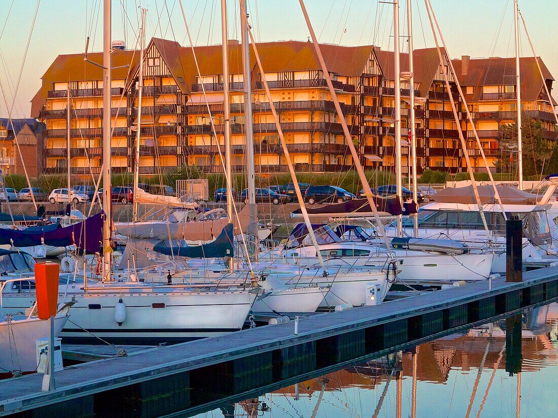 Port Deauville, Floating quay, and pleasance boats moored, with contemporary flats in norman style, in the background, sea front, at sunset, Deauville, Calvados, France.