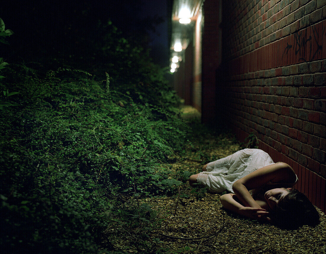 Woman lying by brick wall at night