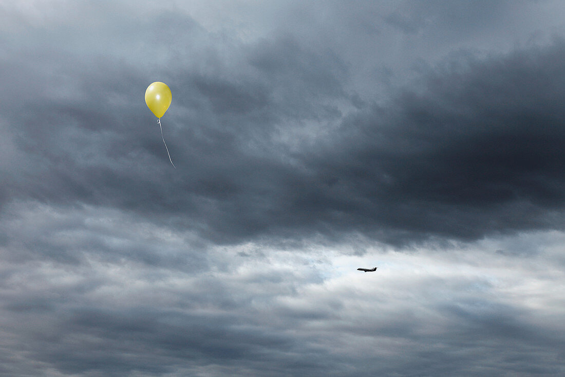 Yellow balloon floating toward cloudy sky