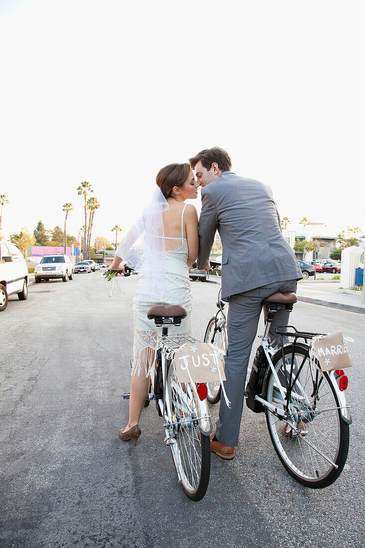 Young newlywed couple kissing on bicycles in street