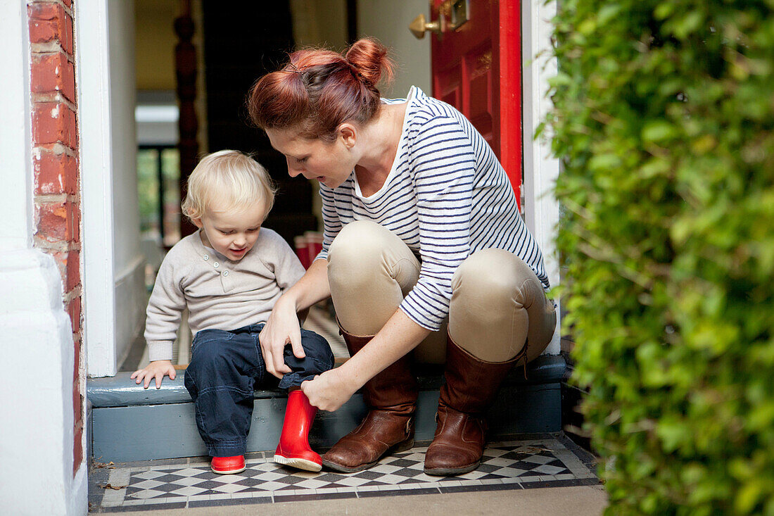 Mother helping toddler son put on rubber boots