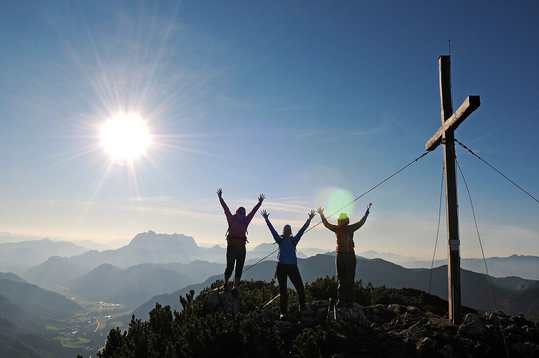 Female hikers cheering beside summit cross on mount Steinplatte, Waidring, Tyrol, Austria