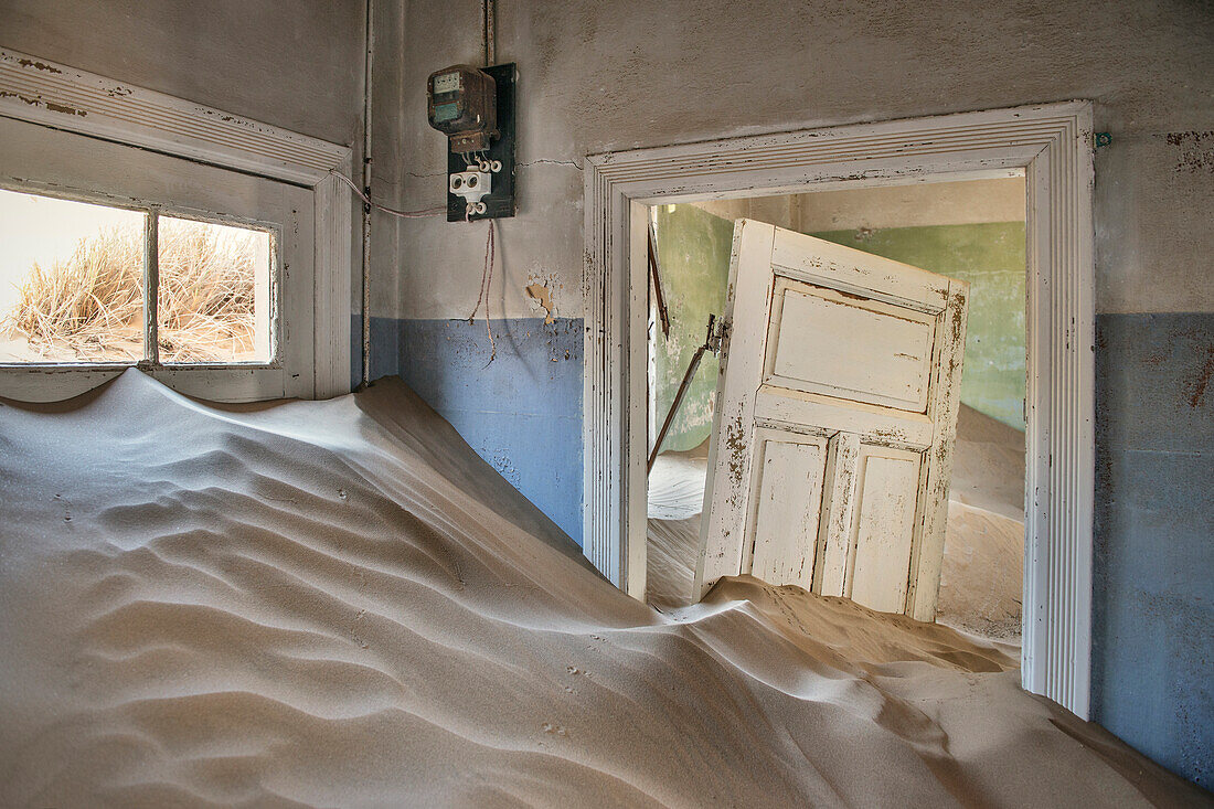 Tür und Stromzähler umschlossen von Dünen, Innenansicht verlassene Geisterstadt im Diamanten Sperrgebiet, Kolmannskuppe bei Lüderitz, Namibia, Afrika