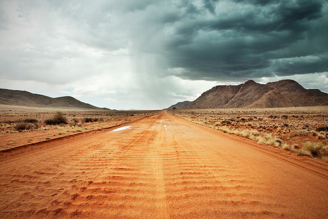 Red sandy road with heavy rainfall and thunderstorm in the distance, Tiras Mountain Range, Namib Naukluft National Park, Namibia, Africa