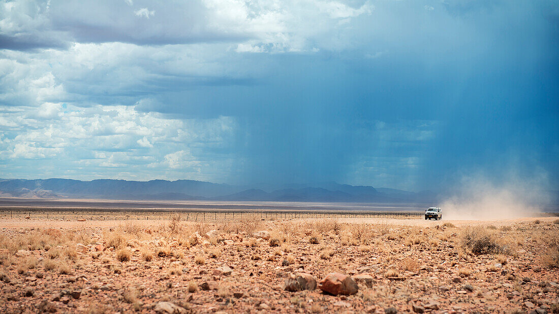 4x4 vehicle driving along a dusty road in the Tiras Mountains, heavy rainfall and thunderstorm in the background, Namib Naukluft National Park, Namibia, Africa