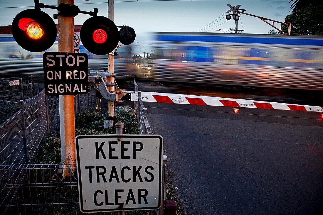 Passenger train moving rapidly through railway crossing with warning lights flashing, Melbourne Australia