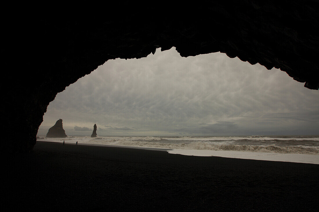 People In The Distance On A Black Sand Beach With Storm Clouds Above, Near Vik, Iceland