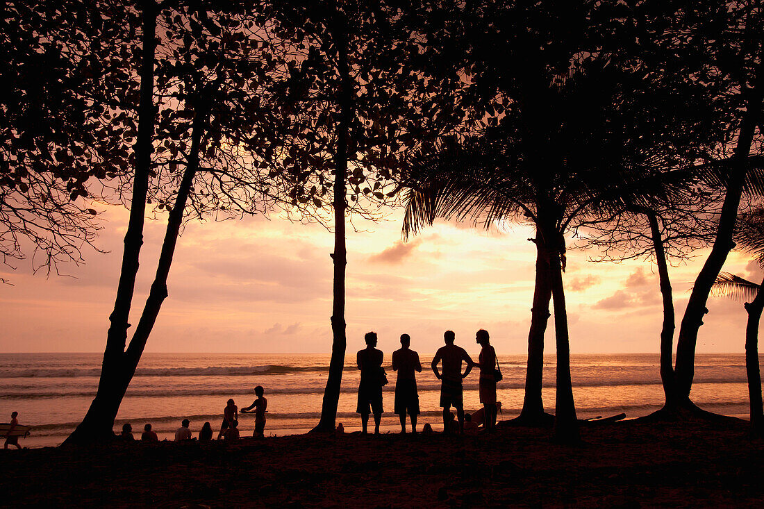'A Group Of People Stand On Santa Teresa Beach Or Playa Santa Teresa Near Mal Pais (Malpais) At Sunset On The Nicoya Peninsula; Puntarenas Province, Costa Rica'