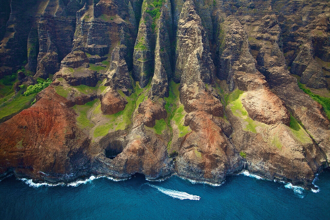'Aerial view of the rugged coastline and a boat in the pacific ocean along an hawaiian island; Hawaii, United States of America'