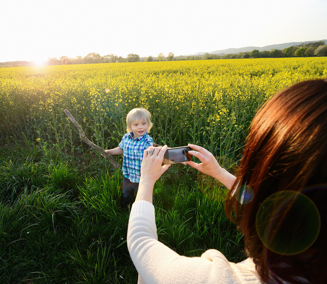 Mother photographing son on smartphone in field