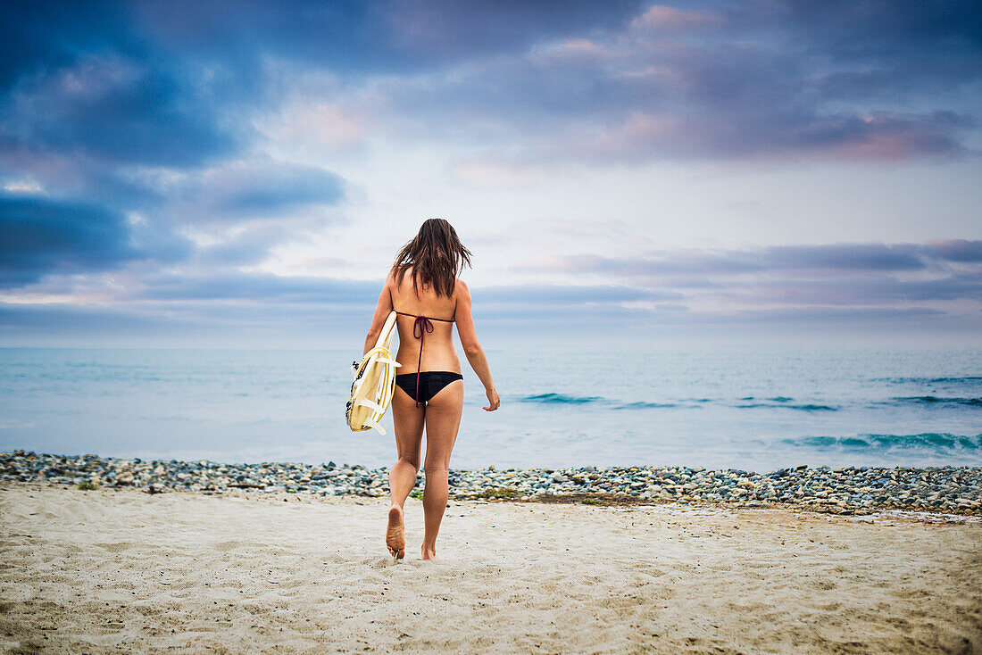 Junge Frau trägt Surfbrett ins Meer