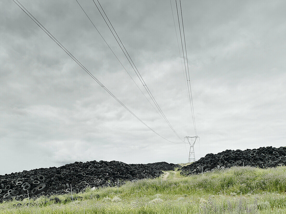 Pile of old tyres under pylon in field