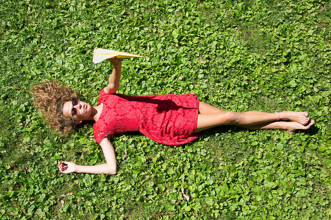 Teenage girl lying on grass holding paper airplane