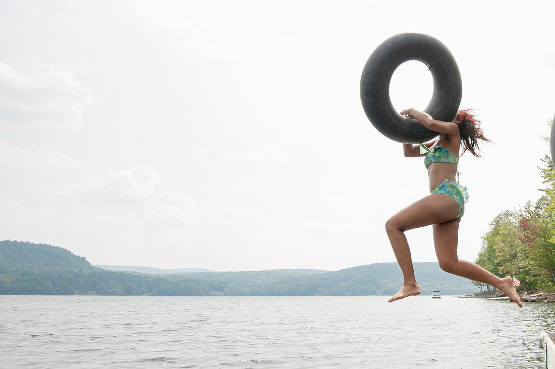 Young woman jumping into lake holding inflatable ring
