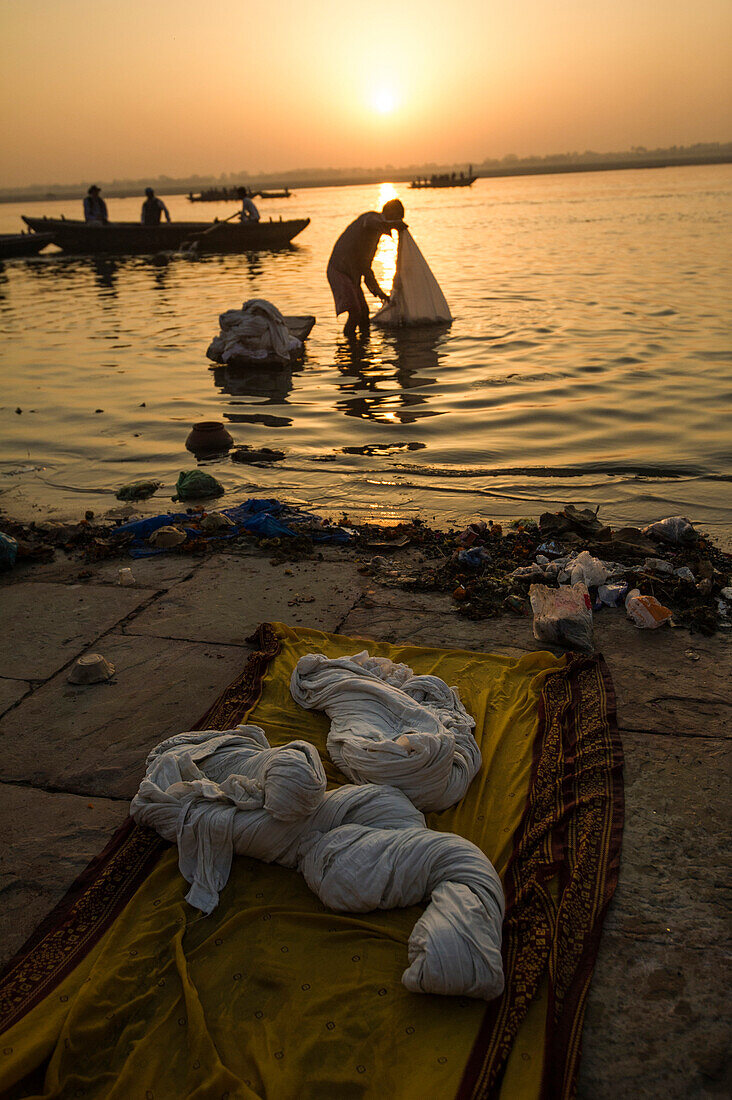 Silhouette of a man washing cloths in the Ganges river at sunrise white boats pass and the sun is rising in the background, Varanasi, India