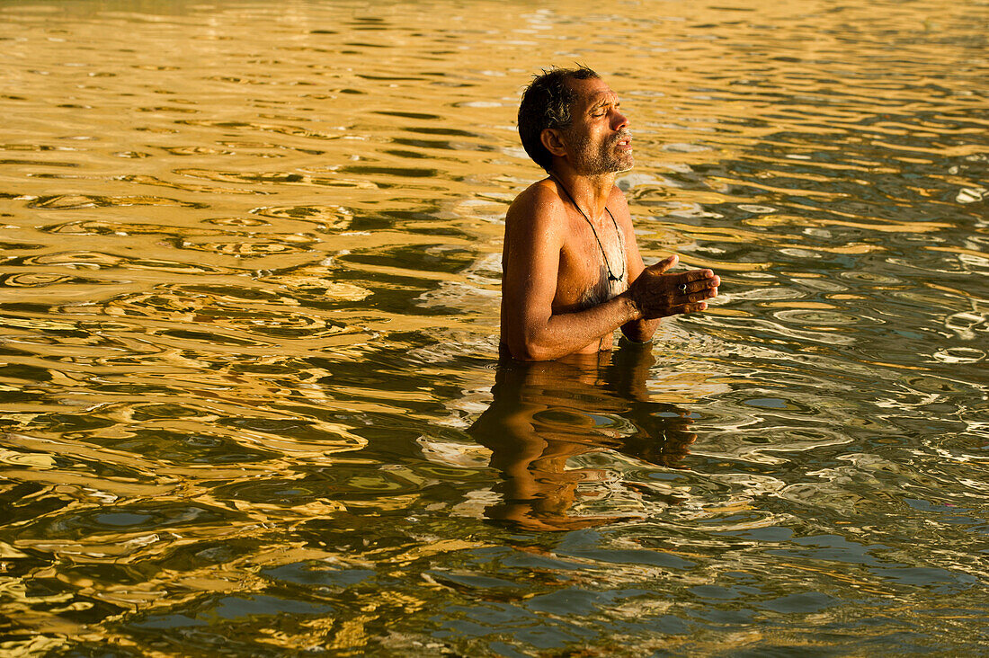 Devotee with hands folded praying in the yellowish waters of the Ganges river on sunrise in Varanasi, India