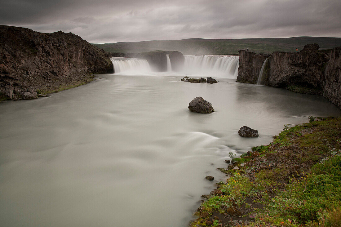 Godafoss waterfall falls into the Skjálfandafljót river below under a cloudy sky, Iceland