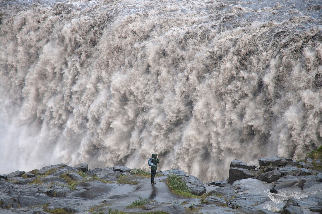 A photographer watches the mighty Dettifoss waterfall falling into the canyon below, Iceland