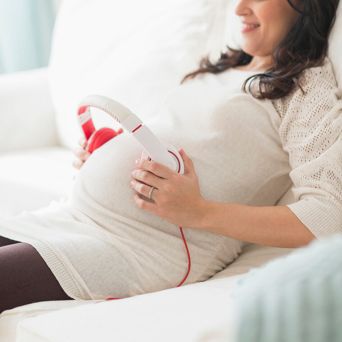 Pregnant Hispanic woman holding headphones on belly, Jersey City, NJ, USA