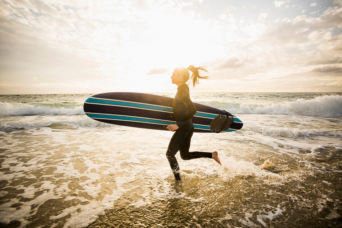 Caucasian surfer carrying board in waves, Los Angeles, California, USA