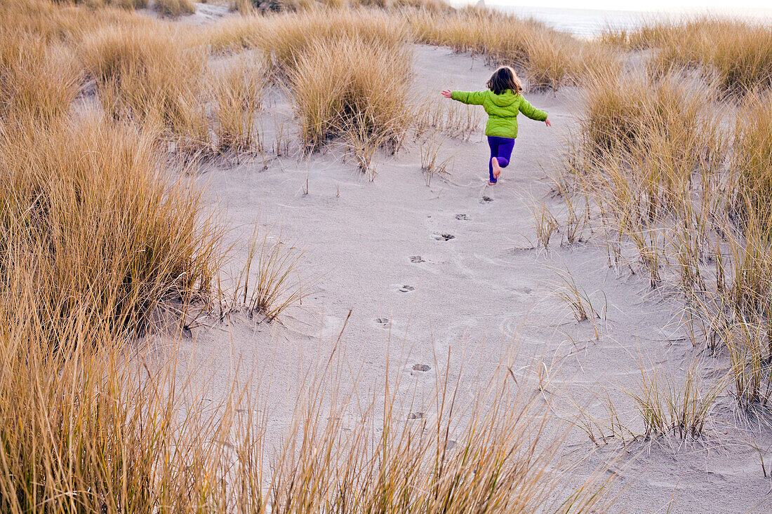 Caucasian girl running on sand dunes, Cannon Beach, Oregon, United States