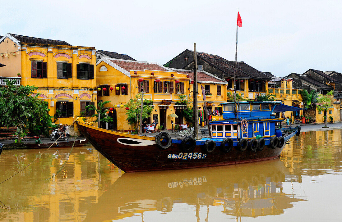 A vietnamese boating in front of yellow houses on the bank of Thu Bon River  in Hoi An, Central Vietnam, South East Asia, Asia