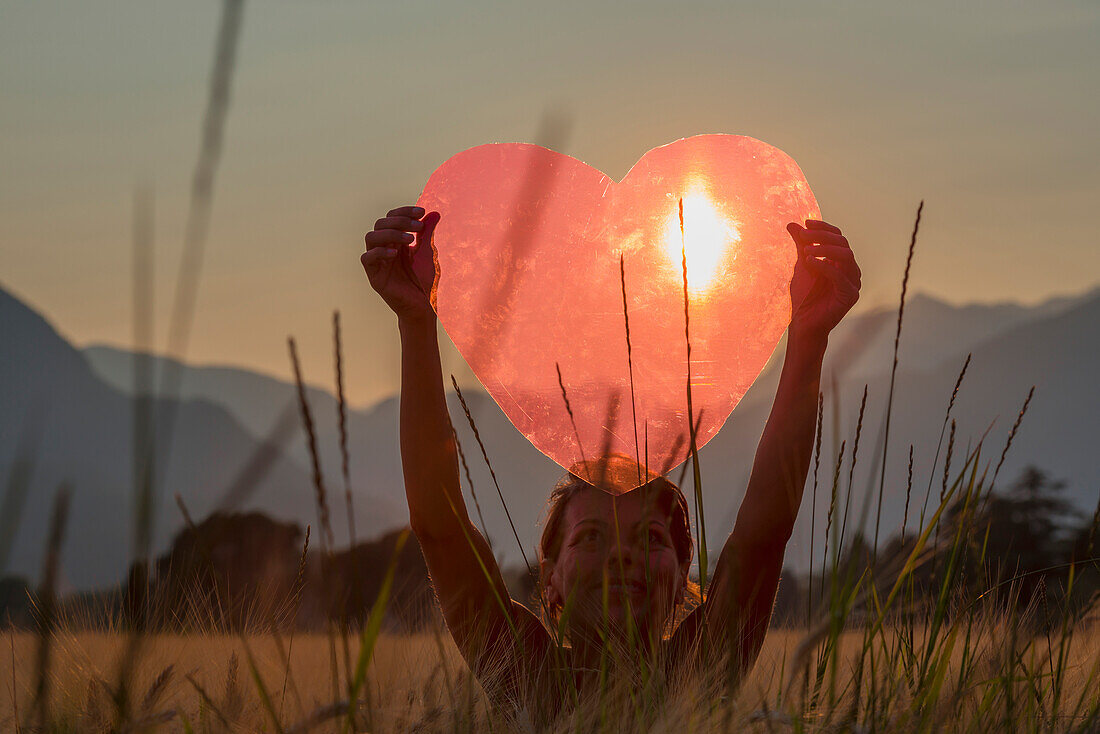 'A Woman Holds Up A Red Heart With The Sun To Shine Through; Locarno, Ticino, Switzerland'