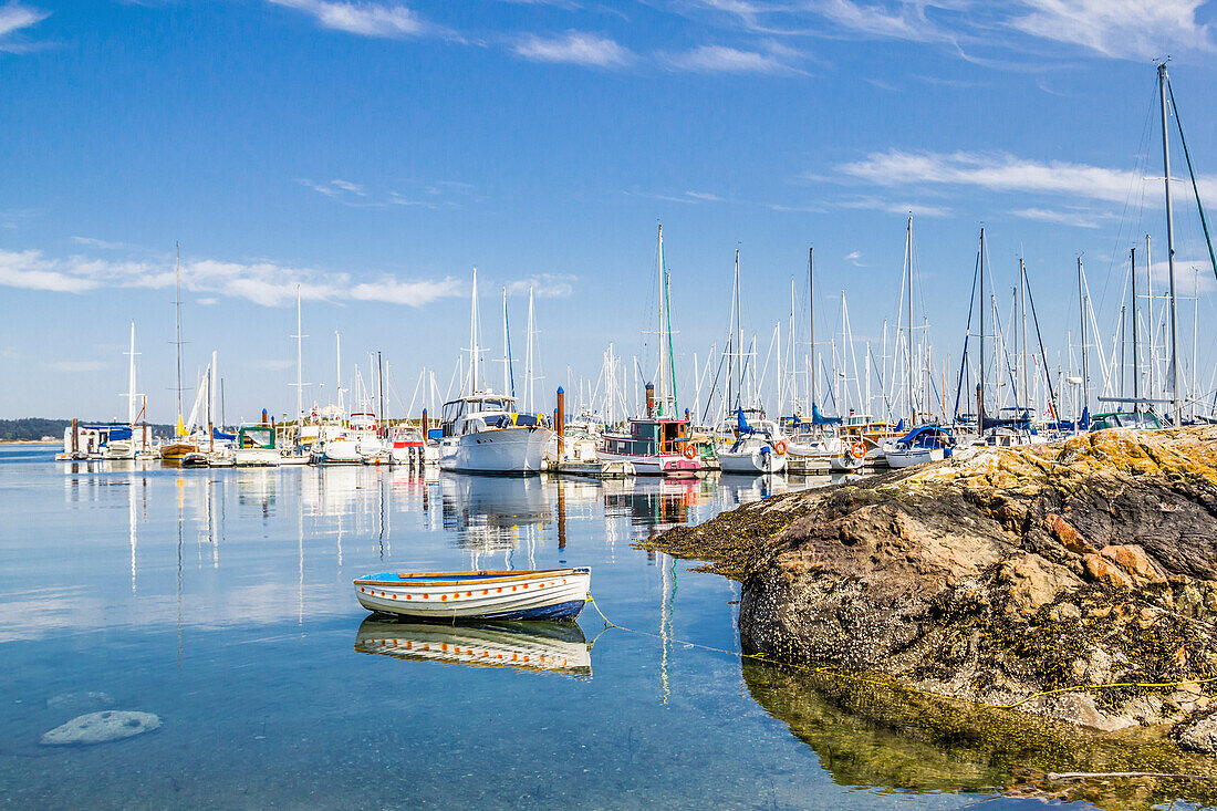 'A row boat is tied to a rock at a recreation marina filled with yachts and sailboats; Victoria, British Columbia, Canada'