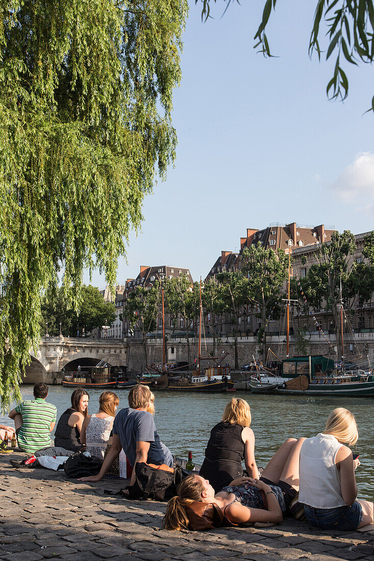 Relaxing and picnicking on the quays of the seine, ile de la cite with the pont neuf bridge and sailboats in front of the square du vert galant, quay of the louvre, paris (75), france