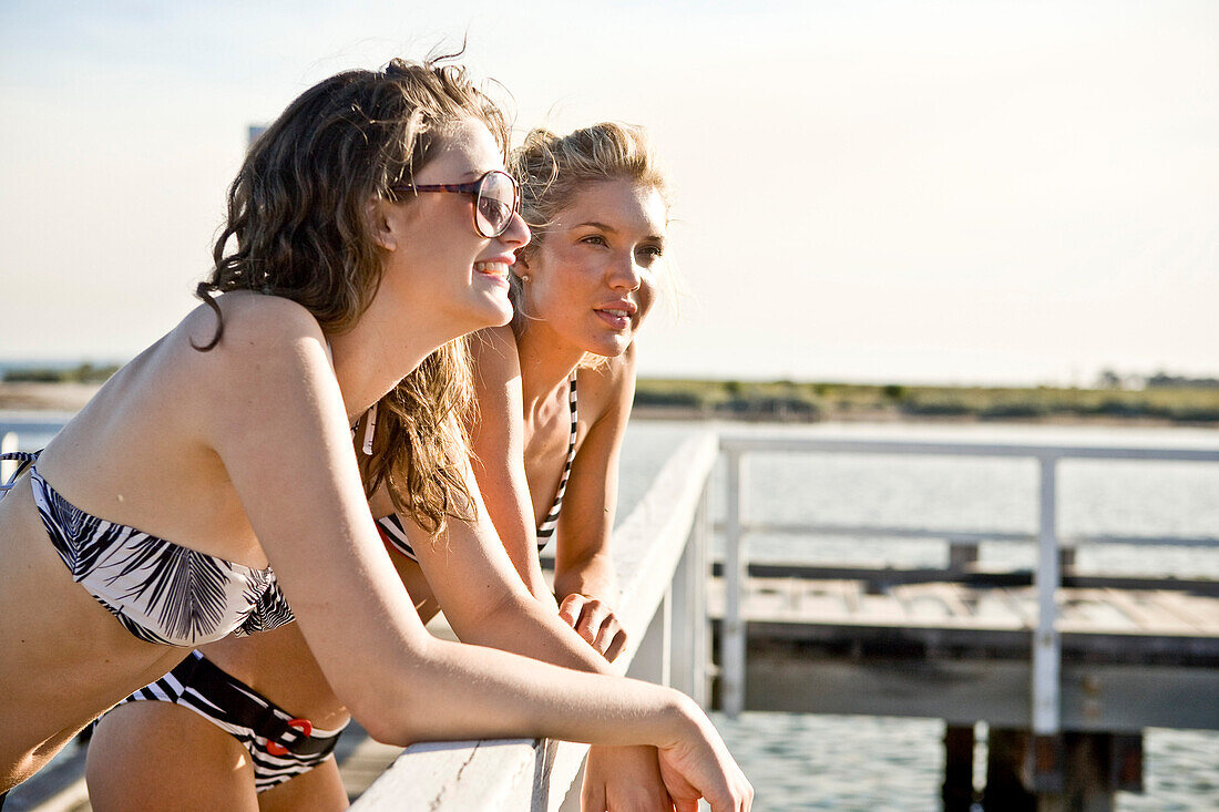 Two Young Women Leaning on Railing on Side of Pier